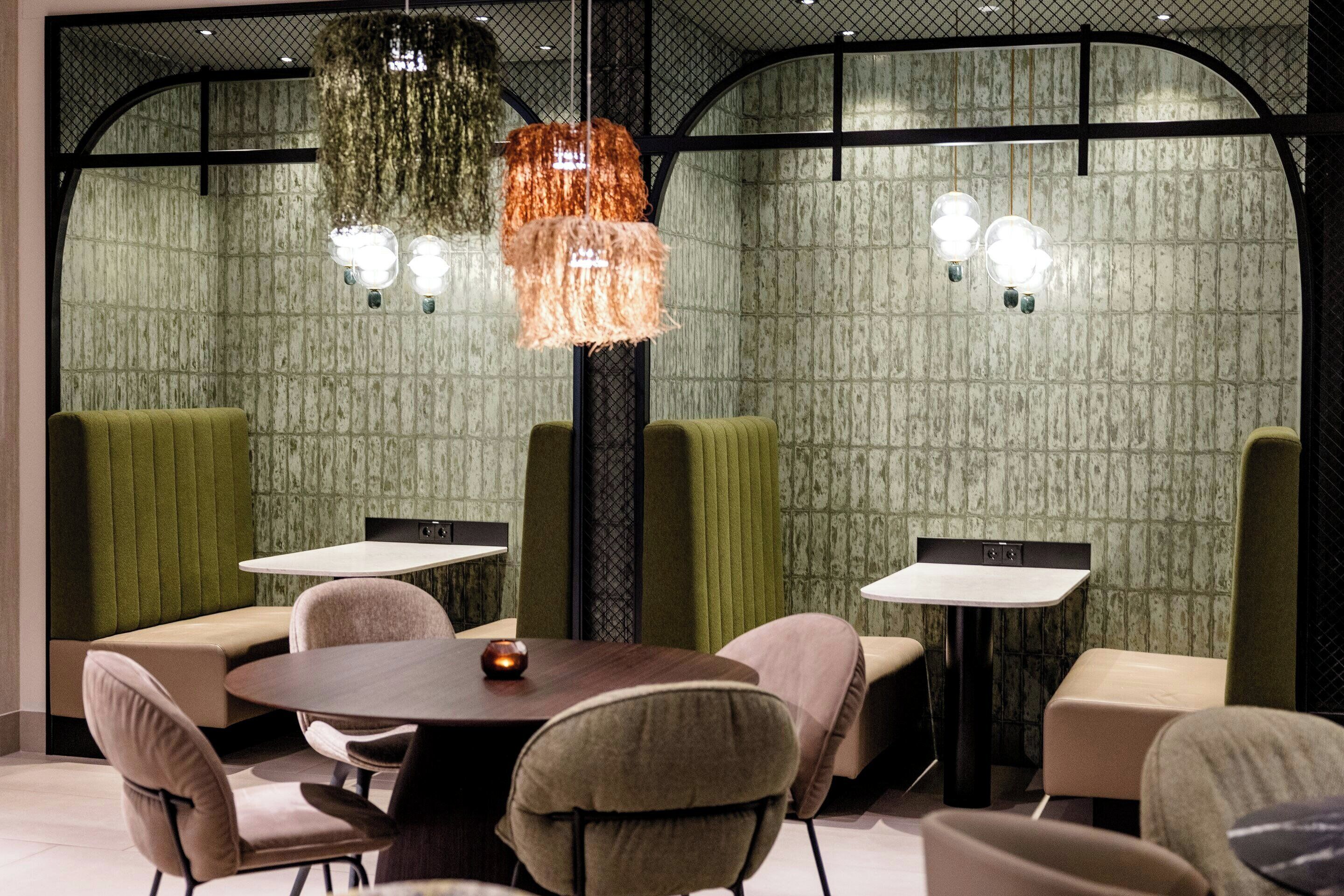 Un espace repas moderne avec des tables rondes et des banquettes rembourrées, agrémenté de papier peint à motifs et de luminaires suspendus originaux.