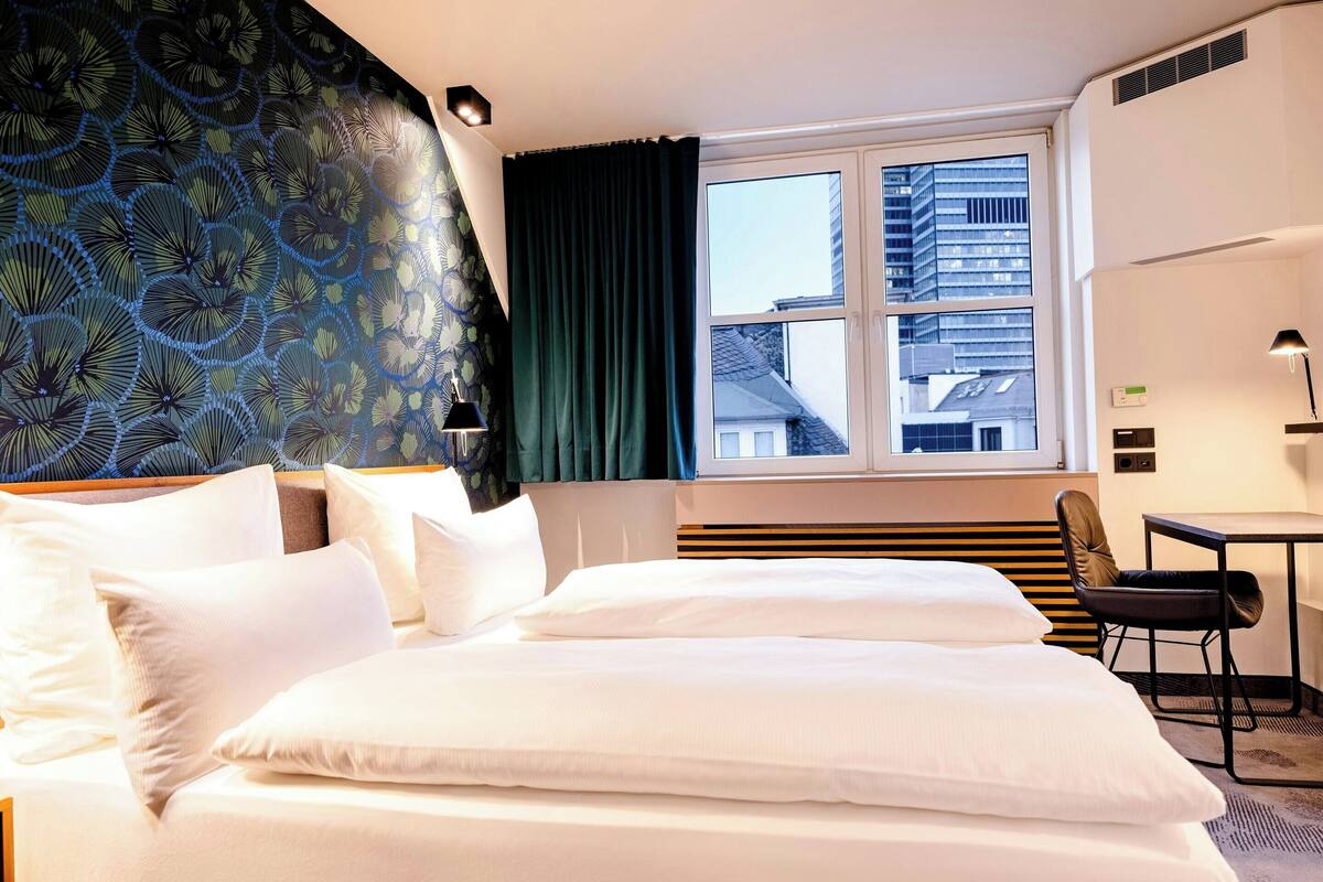 Una camera d'albergo con un letto, una scrivania e una finestra vista edifici.
