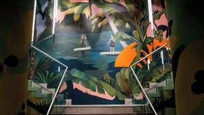 Una escalera con un mural que muestra una escena tropical, con palmeras y una masa de agua.