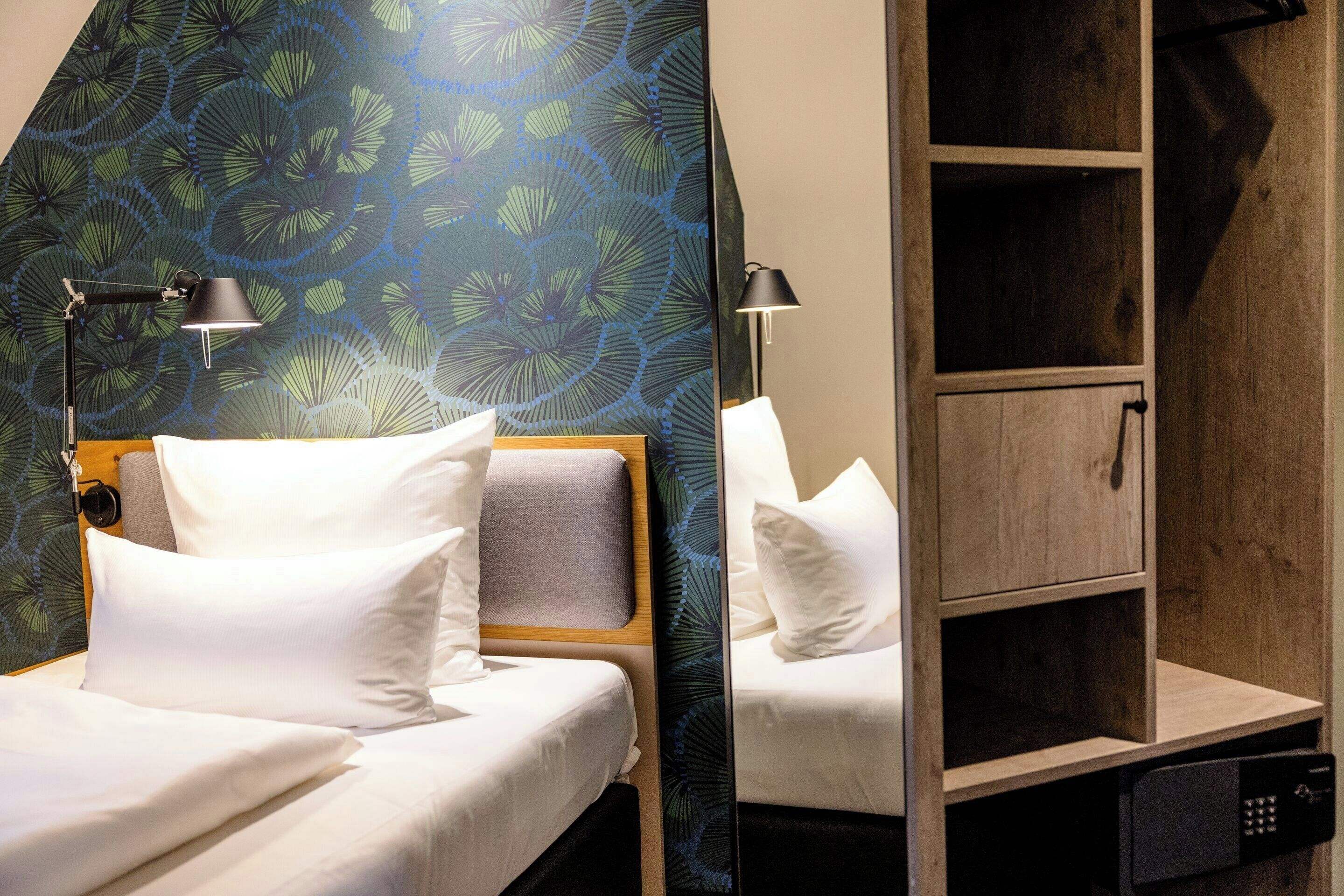 Ein Hotelzimmer mit einem Bett, zwei Nachttischlampen, einem hölzernen Kopfteil, einem Spiegel und einem Schrank aus Holz.