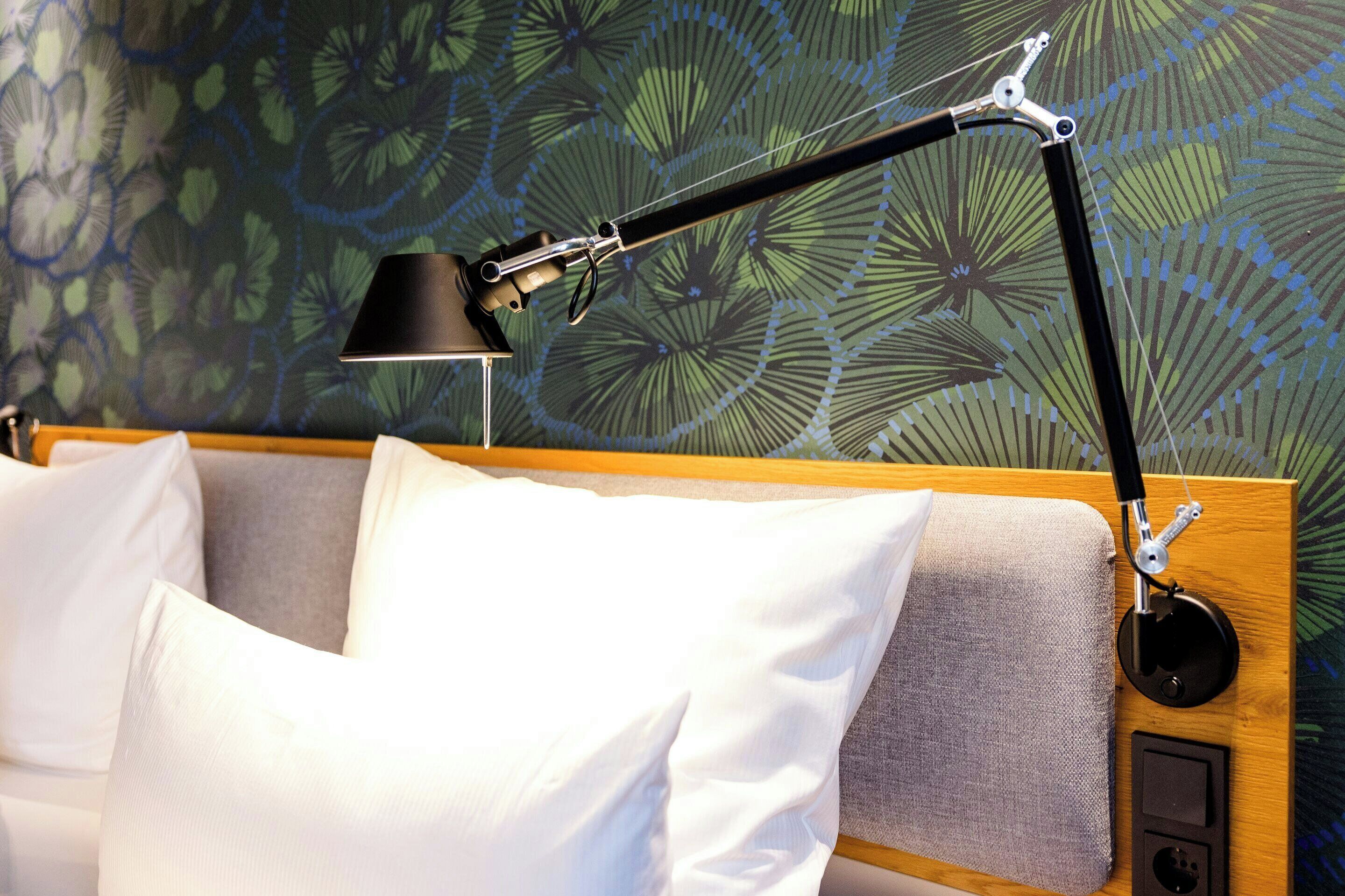 A bed with white pillows, a wooden headboard, and a black adjustable desk lamp.