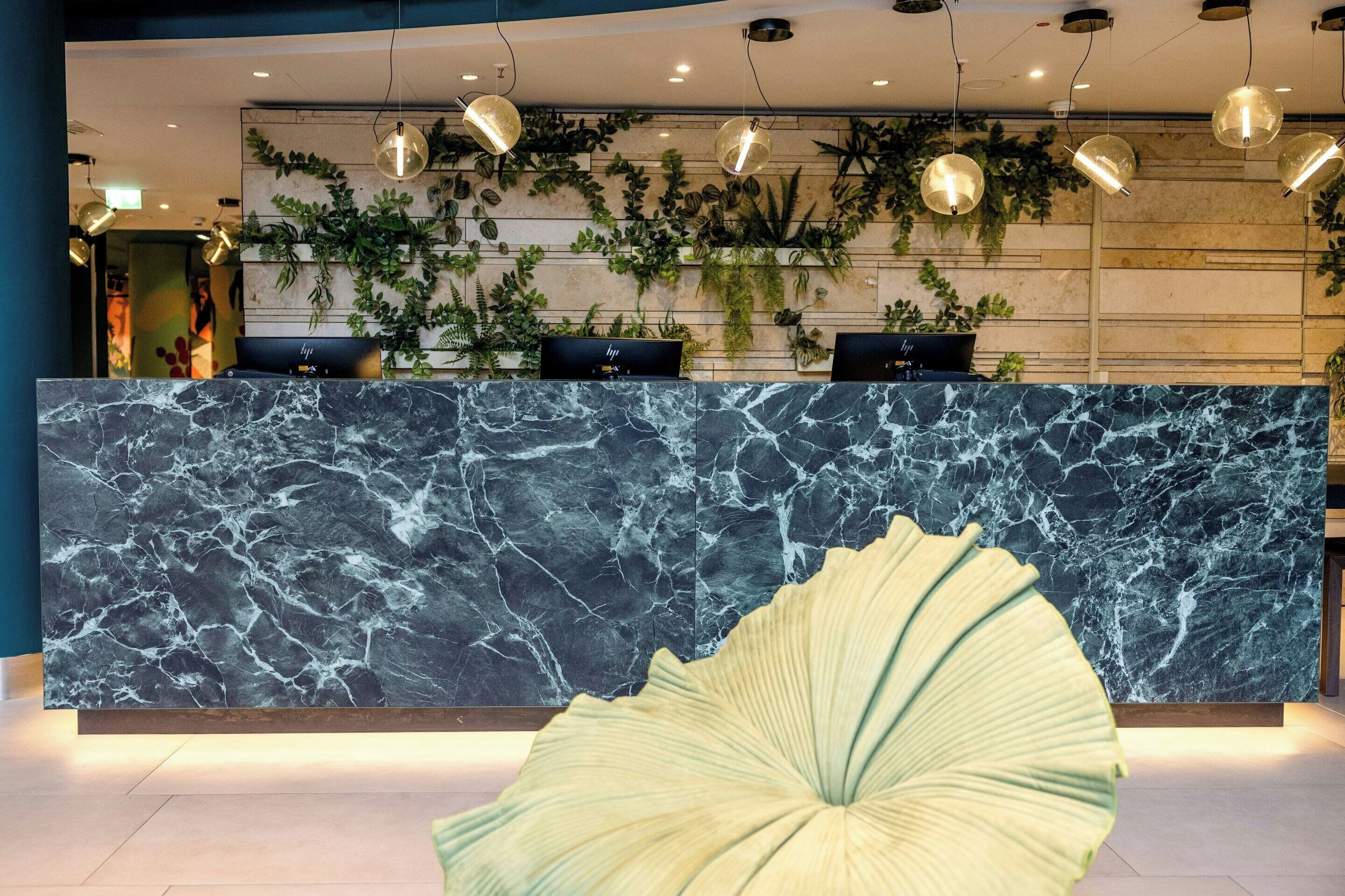 A reception desk with a marble top, surrounded by hanging pendant lights and green plants.