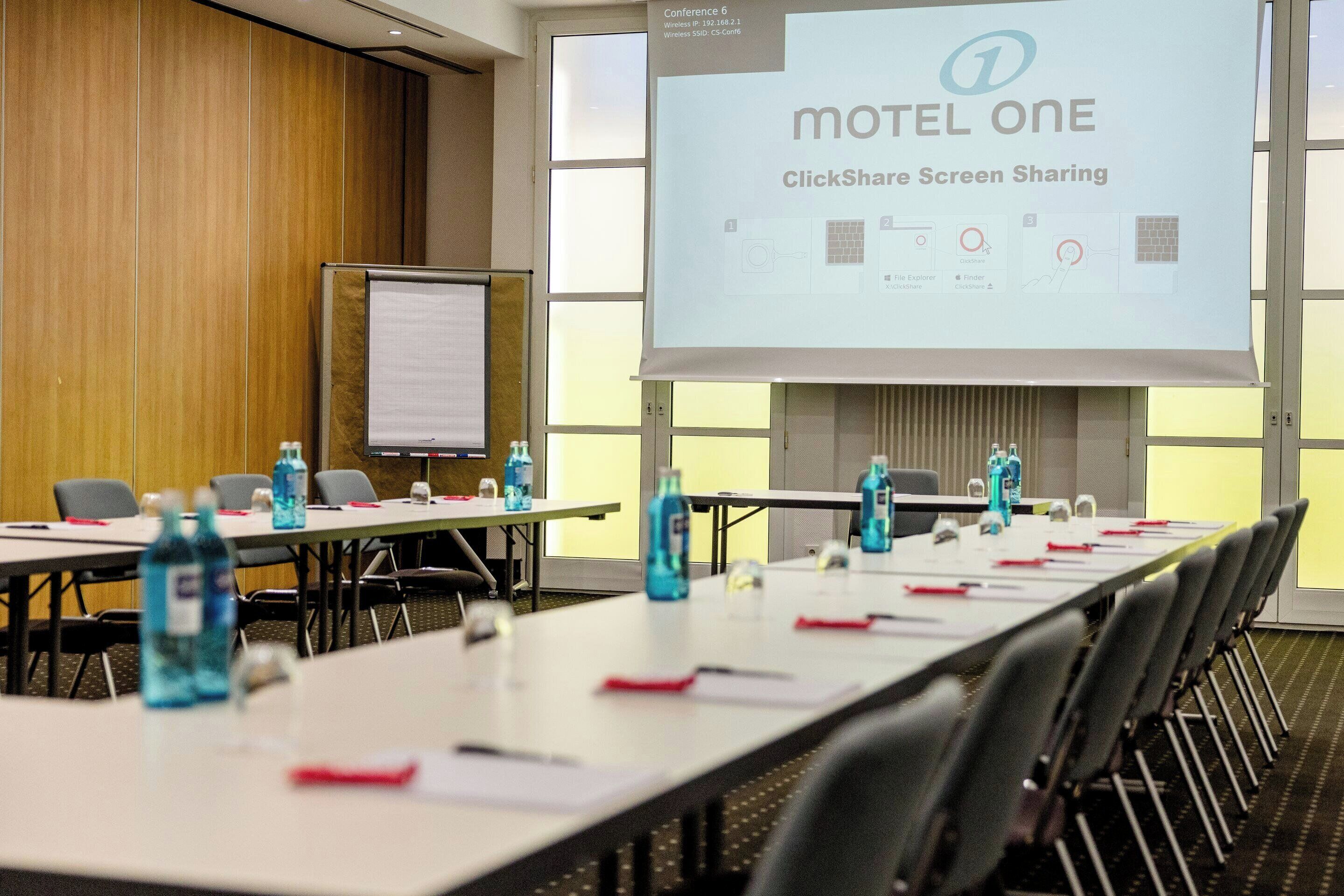 Une salle de conférence équipée d’un écran de présentation affichant « Motel One ClickShare – partage d’écran ».
