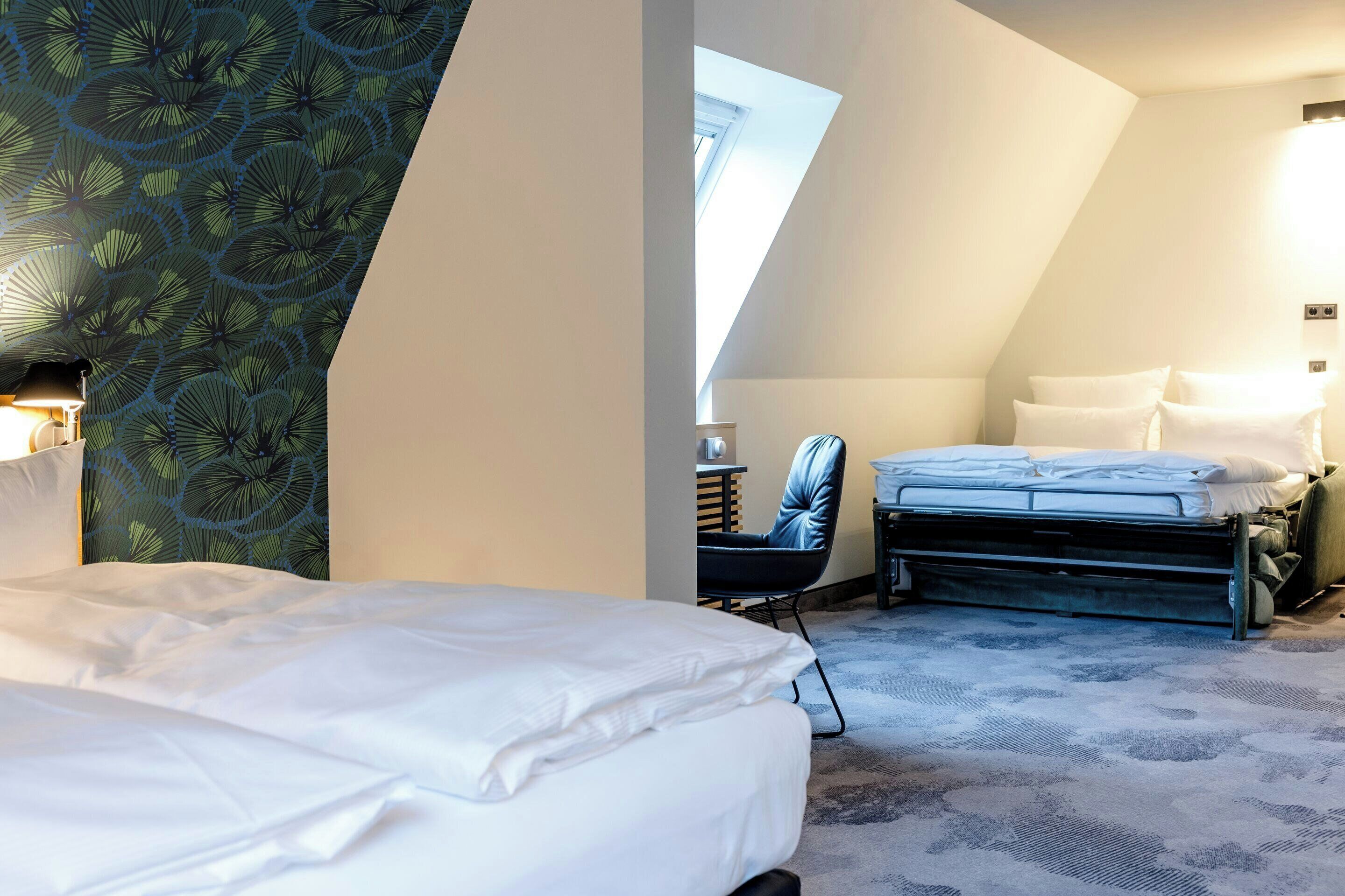 A hotel room with a bed, a chair, a desk, and a skylight.