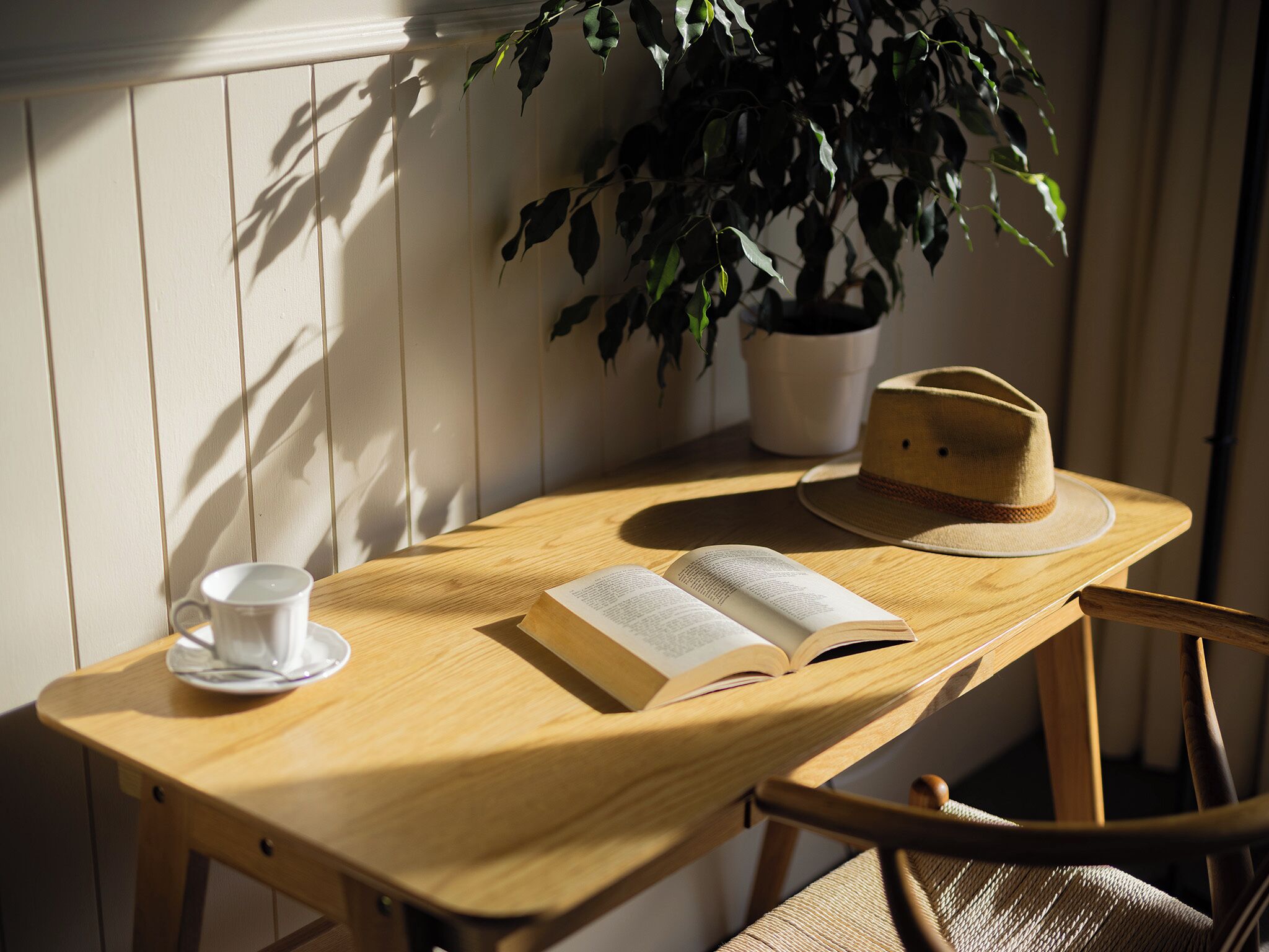 Una mesa de madera con un libro, un sombrero y una taza.