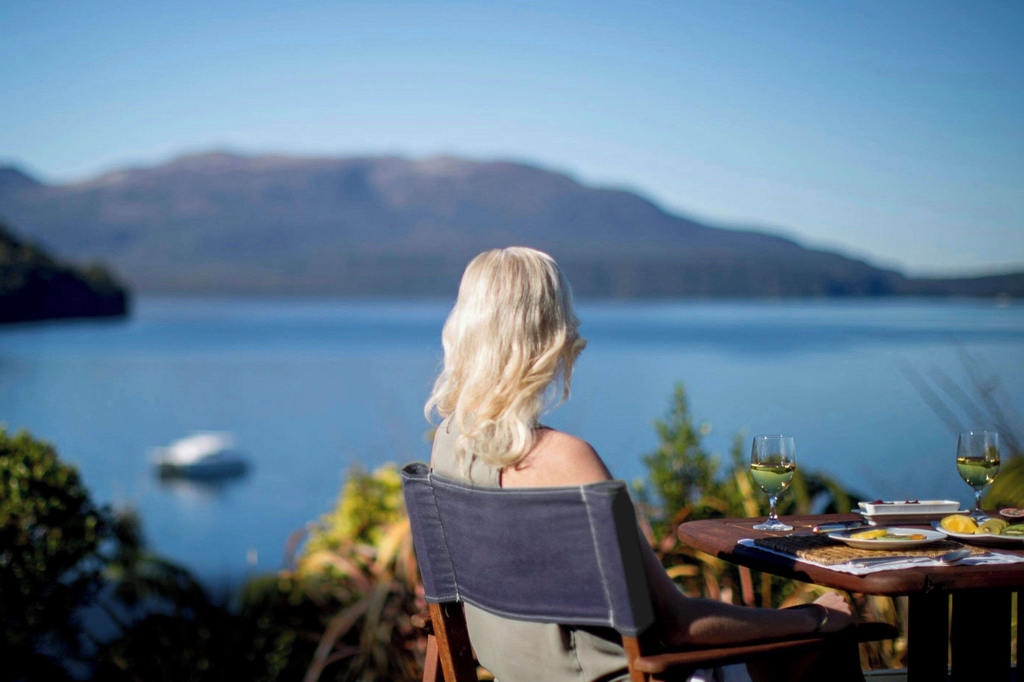 A person seated at a table with a view of a lake and mountains.