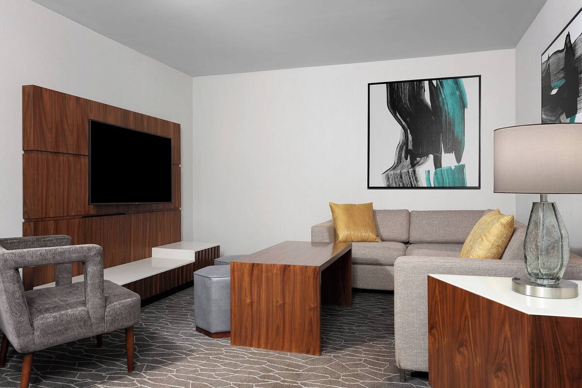 A modern living room with a flat-screen TV, a wooden coffee table, a grey sofa with yellow cushions, and a grey armchair.