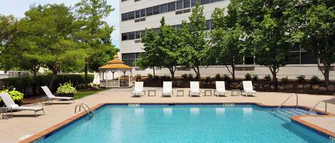 A swimming pool with lounge chairs and a gazebo, surrounded by trees and a building.