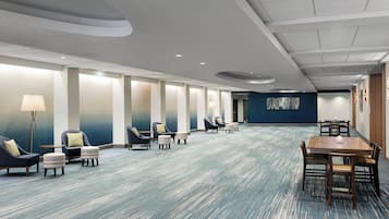 Un hall d’hôtel doté d’un long comptoir d’accueil, de plusieurs espaces de détente avec des fauteuils et des poufs, et d’un sol recouvert de moquette.