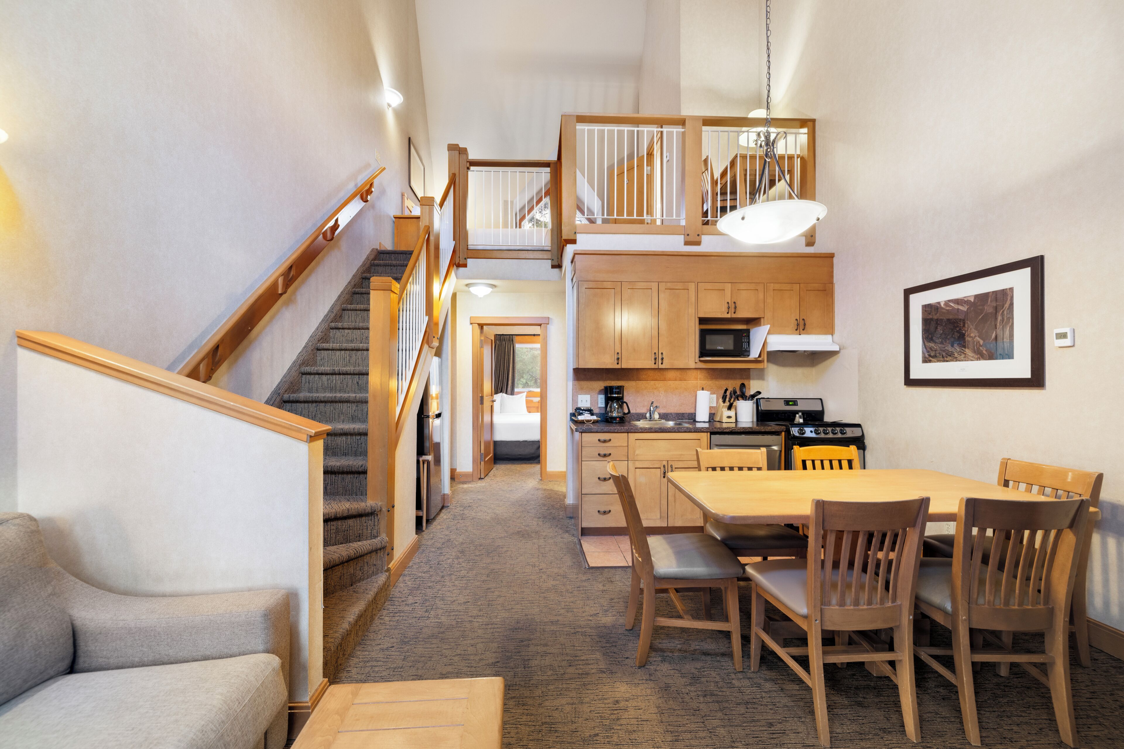 Habitación de hotel compacta con kitchenette, zona de comedor y escalera que conduce a un nivel superior.
