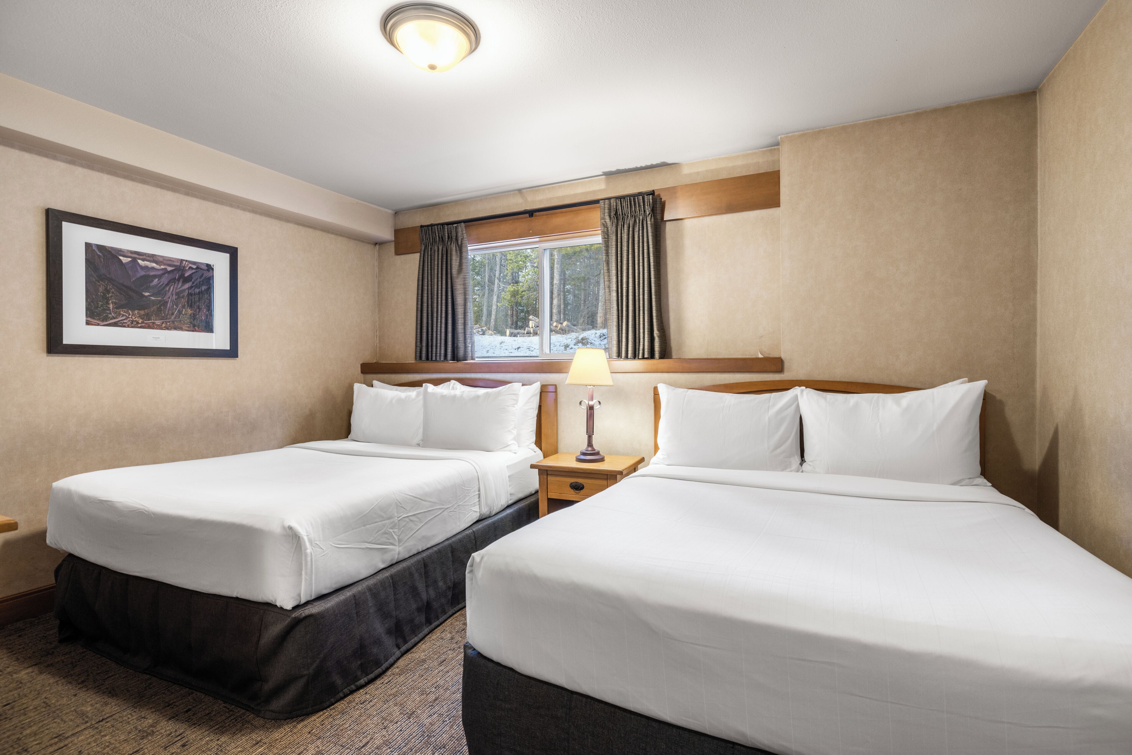 Habitación de hotel con dos camas, una mesita de noche, una lámpara, un cuadro en la pared y una ventana con cortinas.
