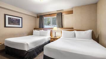 Habitación de hotel con dos camas, una mesita de noche, una lámpara, un cuadro en la pared y una ventana con cortinas.