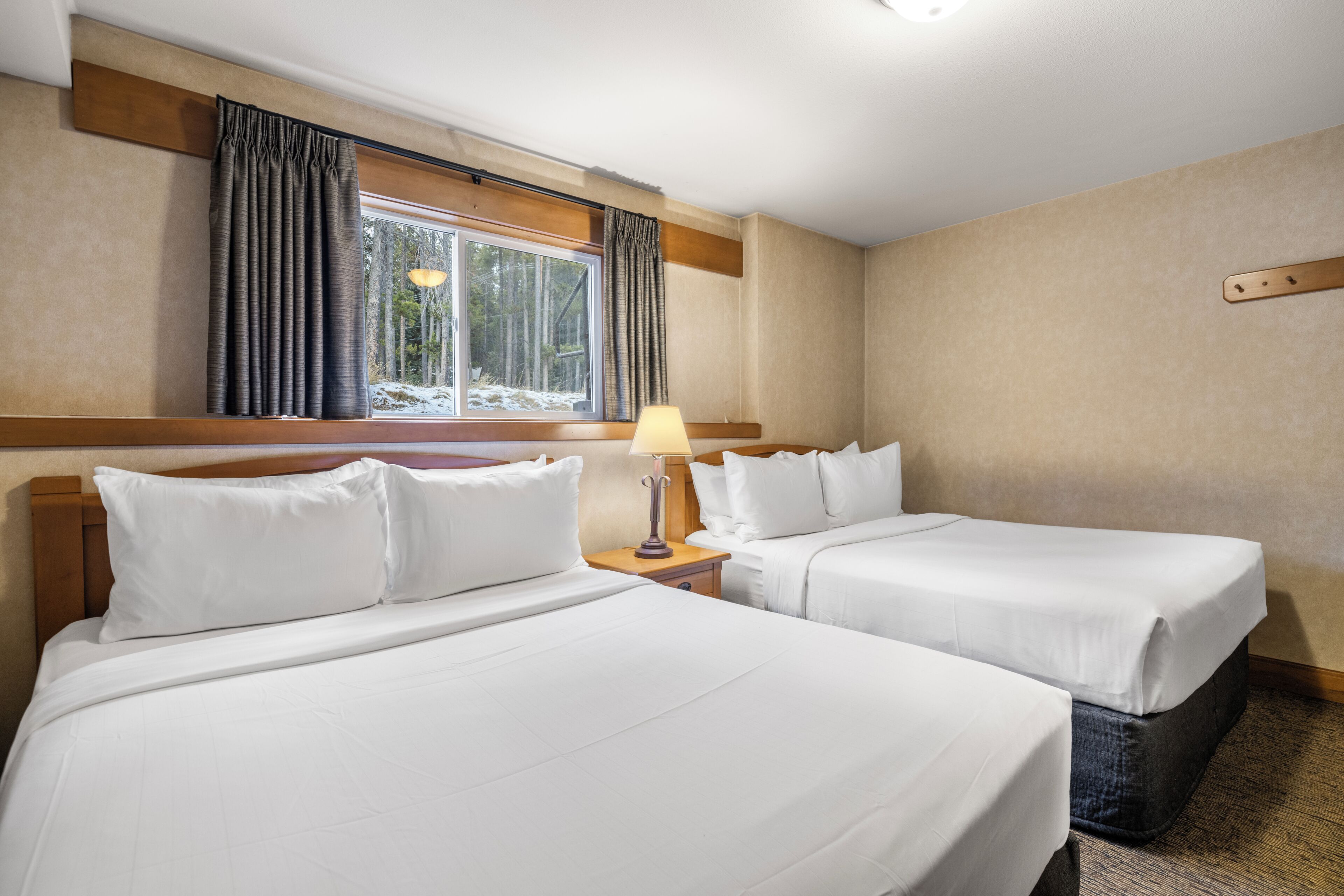 Ein Hotelzimmer mit zwei Betten, einem Nachttisch mit Lampe und einem Fenster mit Vorhängen.