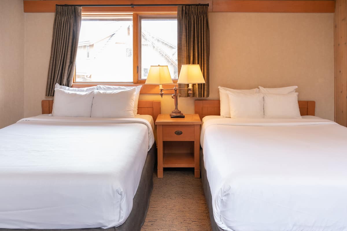 A hotel room with two single beds, a nightstand with a lamp, and a window with curtains.