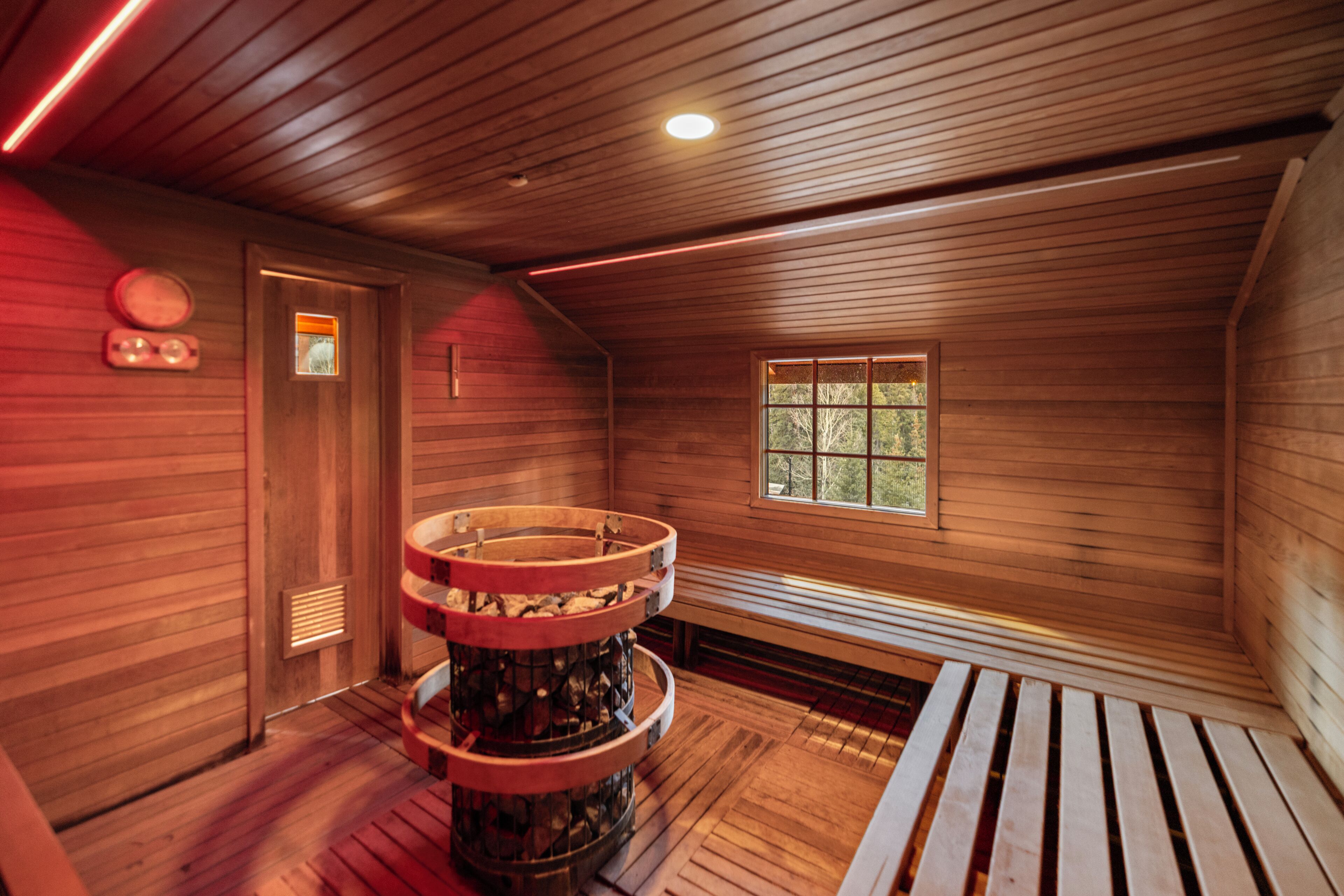 A wooden interior with a circular wooden structure, a window with a view, and a sloped ceiling.