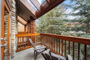 A balcony with wooden railings, a stone wall, and a view of trees.