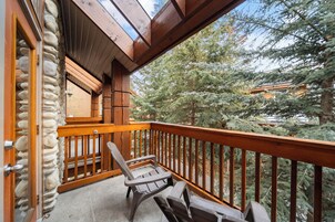 A balcony with wooden railings, a stone wall, and a view of trees.