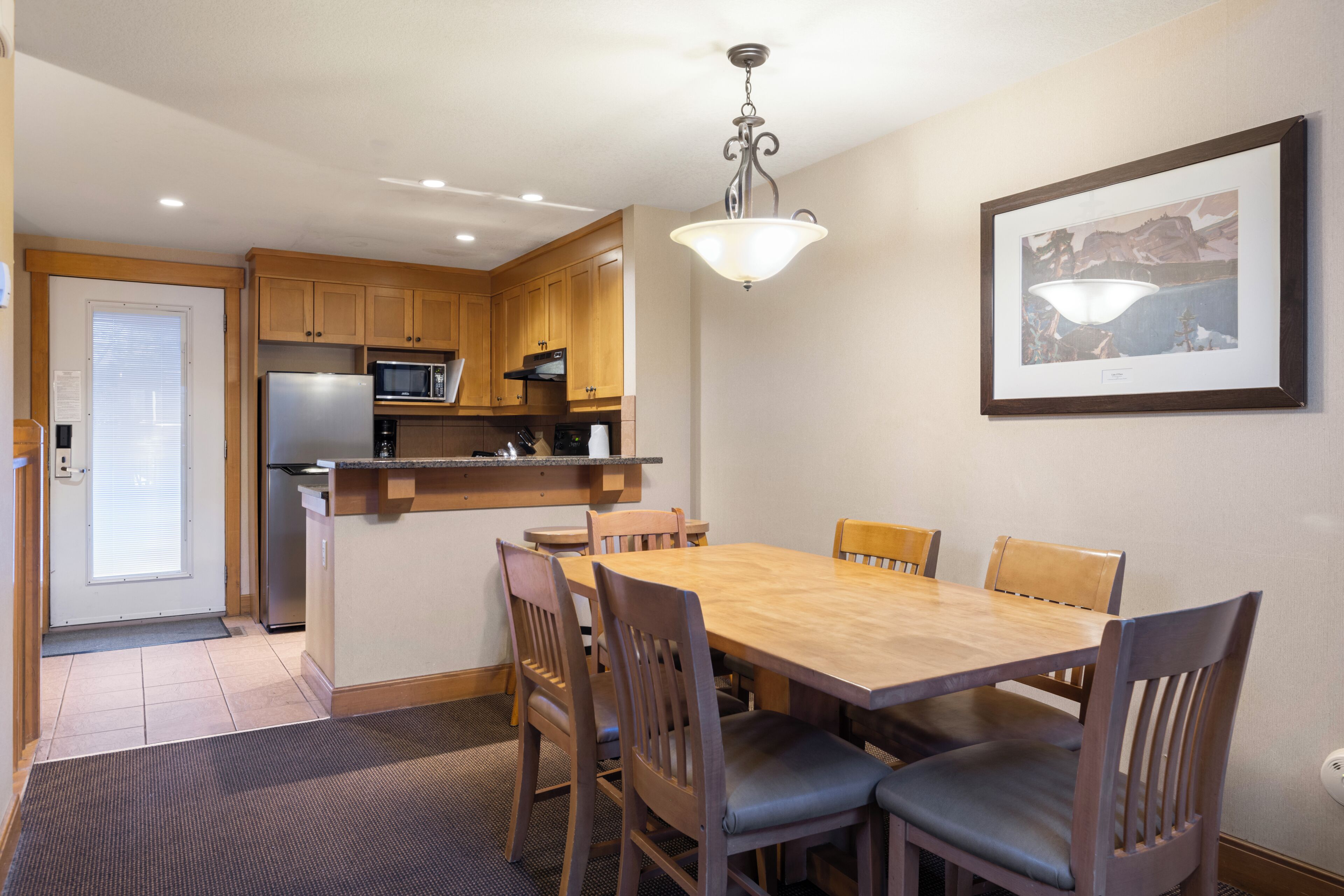 A compact kitchen with wooden cabinets, a built-in microwave, and a dining area with a wooden table and chairs.