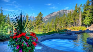 Relax in a serene hot spring surrounded by lush greenery and distant mountains, featuring a clear pool with a tiled edge and natural rock formations.