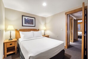 A hotel room with a bed, two bedside lamps, a framed picture on the wall, and a door leading to another room.