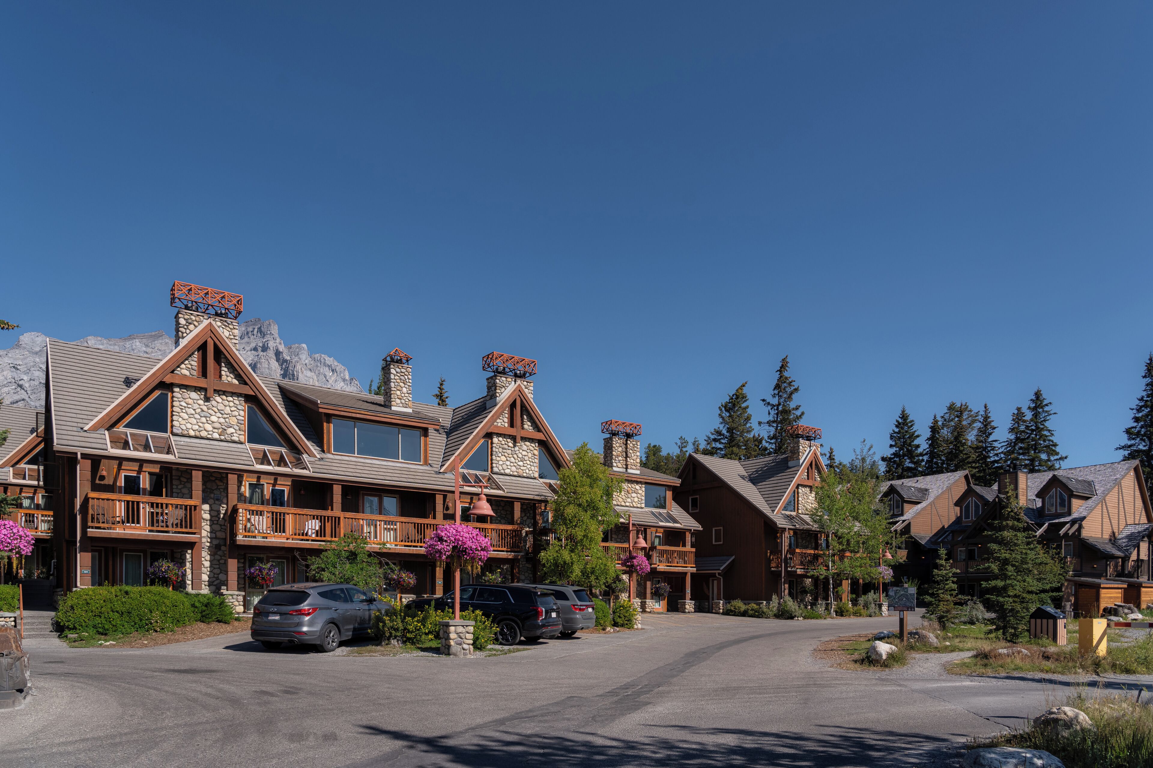 A row of log cabin-style buildings with stone chimneys, wooden balconies, and a clear sky.