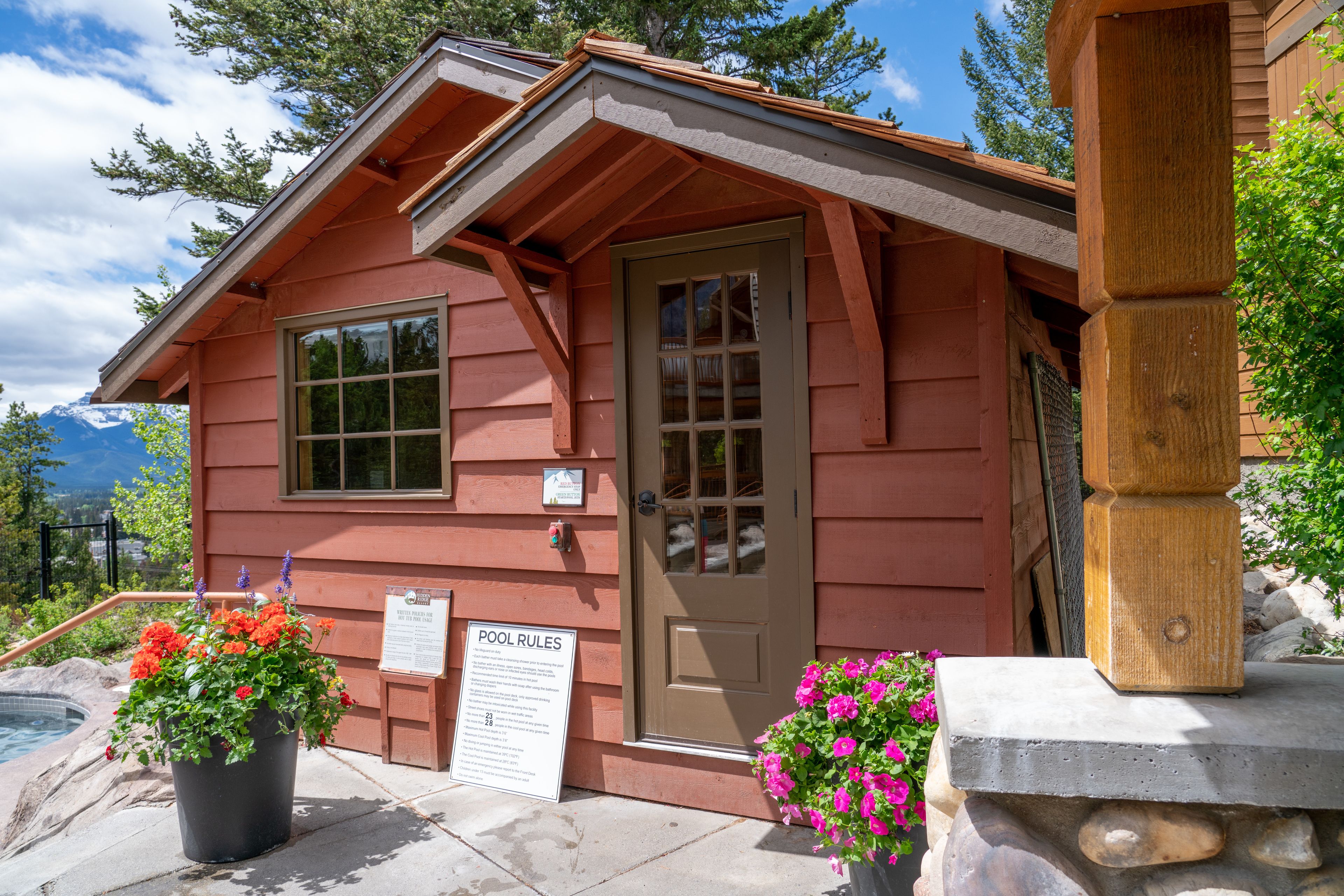A wooden cabin with a pool, a door, and two flower pots.