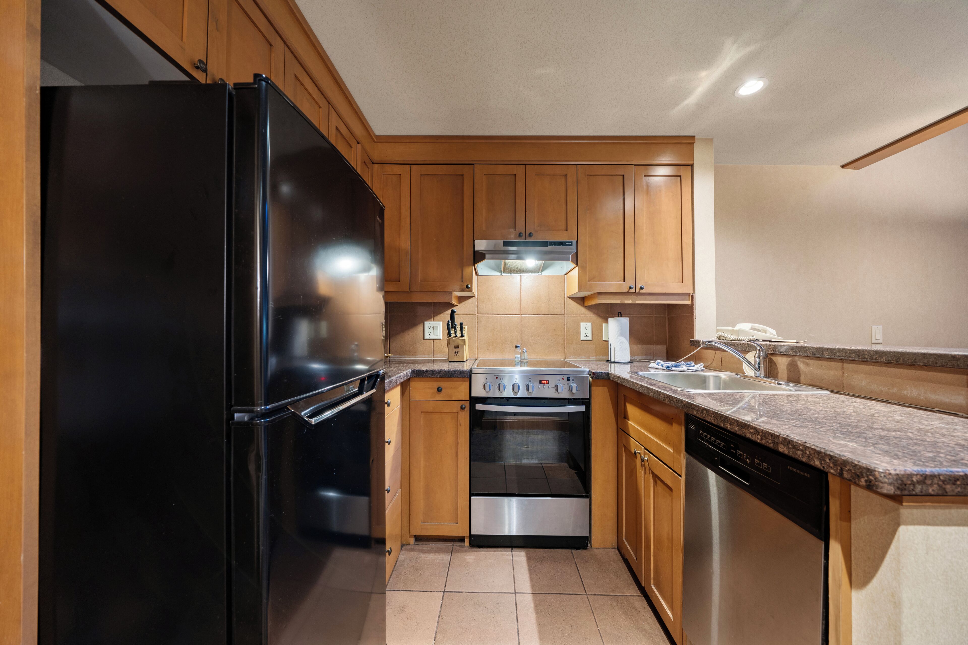 A kitchen with wooden cabinets, a black refrigerator, a stove, and a dishwasher.