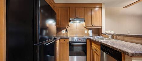 A kitchen with wooden cabinets, a black refrigerator, a stove, and a dishwasher.