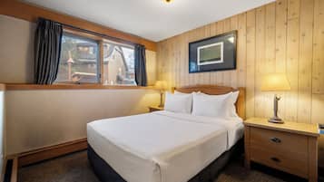 Habitación de hotel con una cama grande, dos mesitas de noche con lámparas, una ventana con cortinas e imagen enmarcadas en la pared.