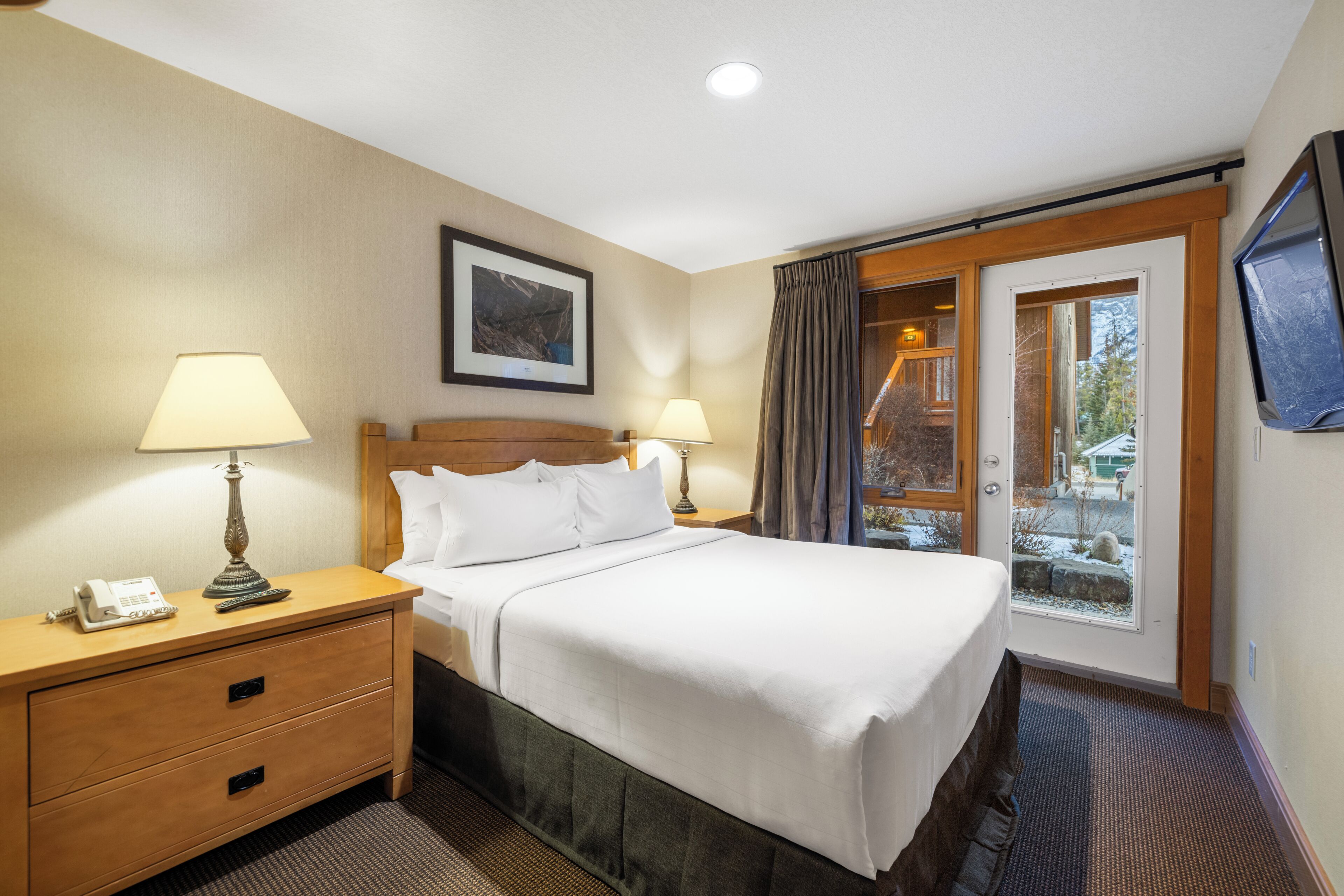 A hotel room with a bed, bedside lamps, a telephone, a framed picture on the wall, and a window with curtains.