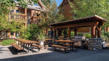 Un patio al aire libre con mesas de picnic y una parrilla, rodeado de muros de piedra y estructuras de madera.