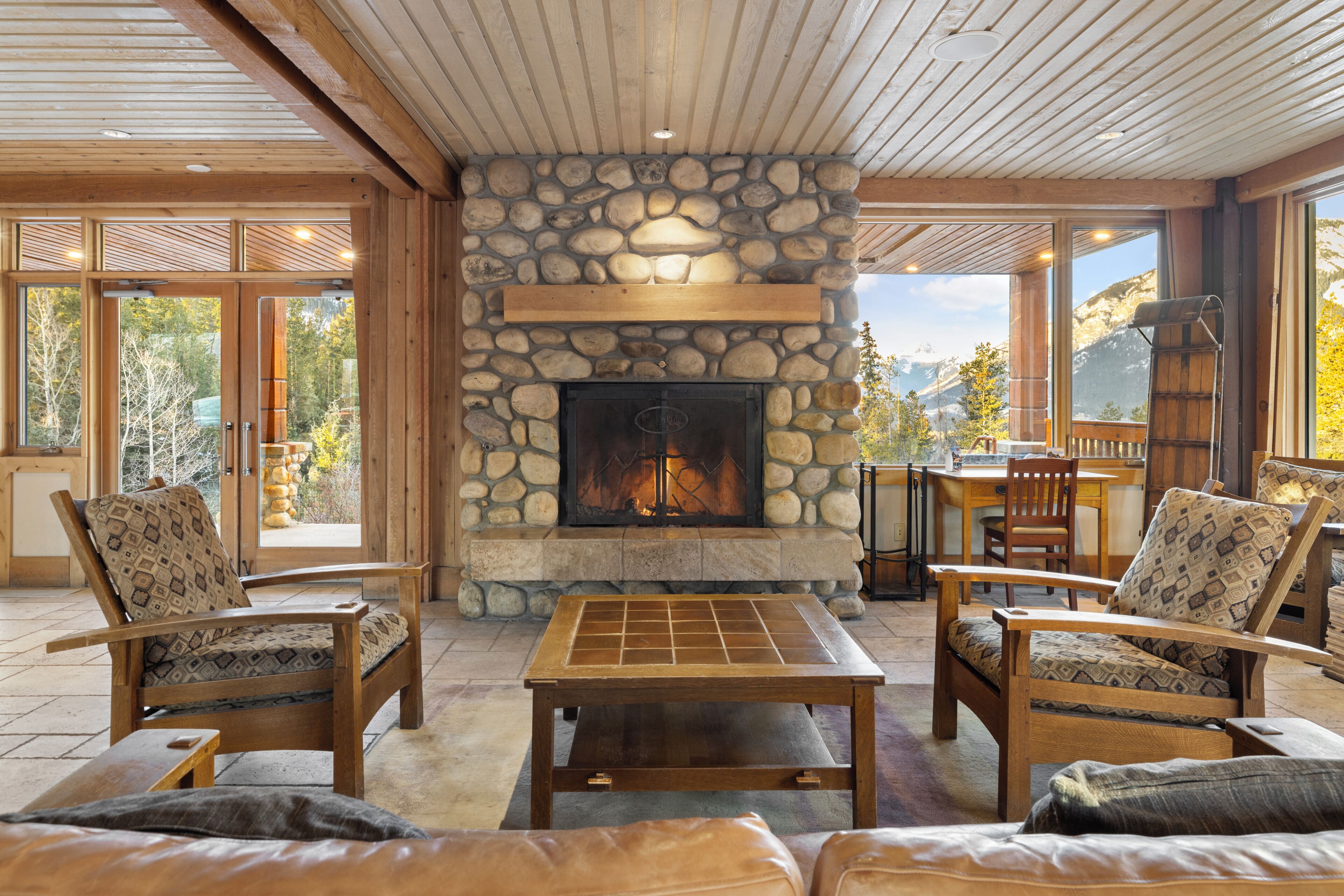 Un interior acogedor con chimenea de piedra, muebles de madera y amplios ventanales que ofrecen vistas al exterior.