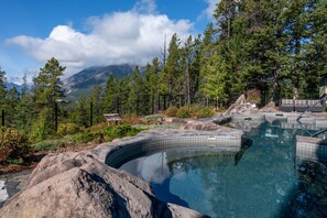 A natural hot spring surrounded by rocks and trees with a mountainous backdrop. - Hidden Ridge Resort (Banff)