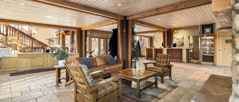 Un vaste espace intérieur doté d’un plafond en bois, d’un canapé, de deux fauteuils, d’une table basse et d’une cheminée en pierre.