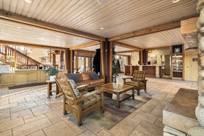 A spacious indoor area with a wooden ceiling, a sofa, two armchairs, a coffee table, and a stone fireplace.
