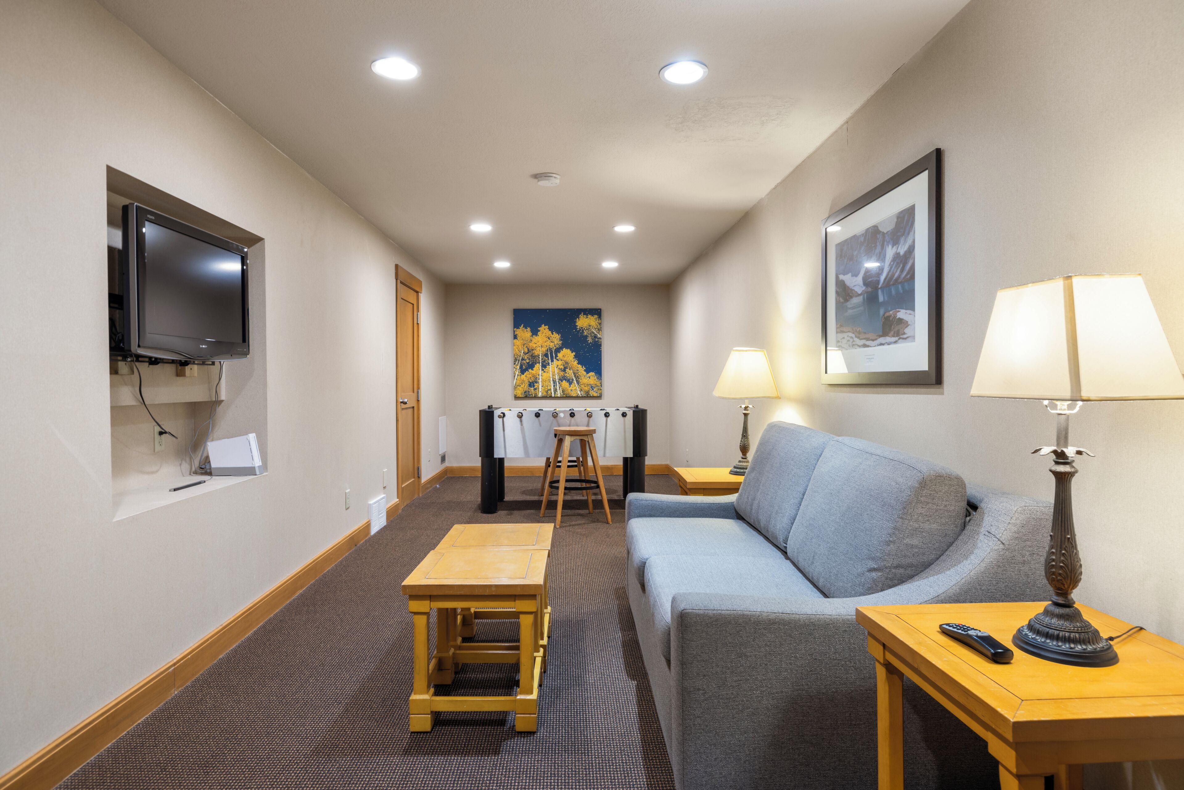 A hotel room with a flat-screen TV, a sofa, a table with a lamp, a framed picture, and a futon.