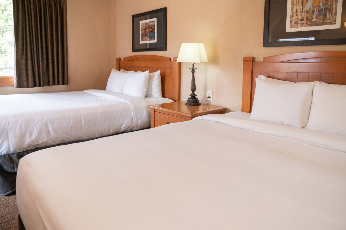 A hotel room with two beds, a nightstand with a lamp, and two framed pictures on the wall.