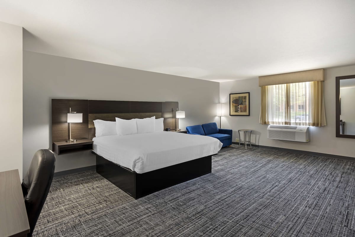 A hotel room with a large bed, a desk, a chair, a blue sofa, and a window with curtains.