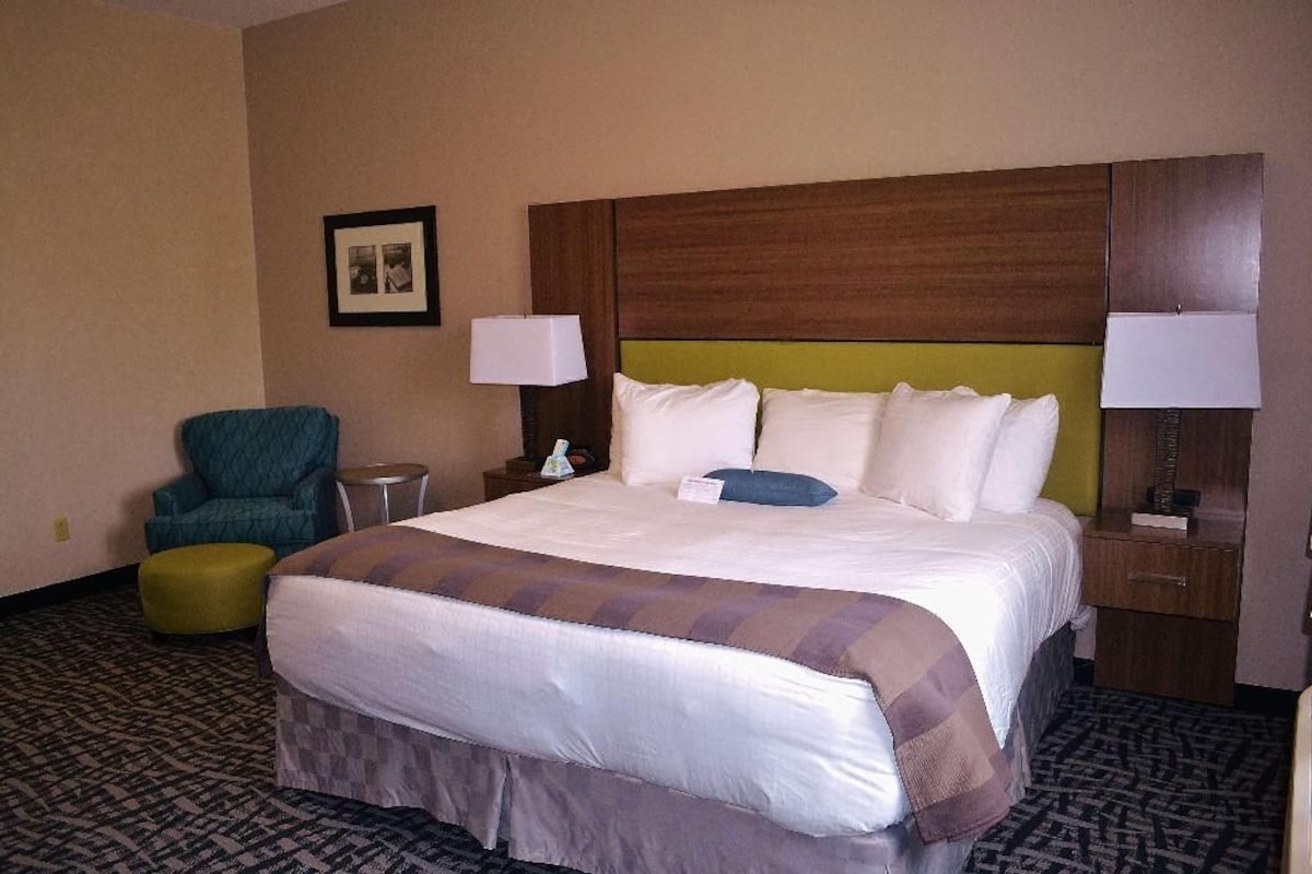 A hotel room with a large bed, two bedside tables, a chair, and a small table.