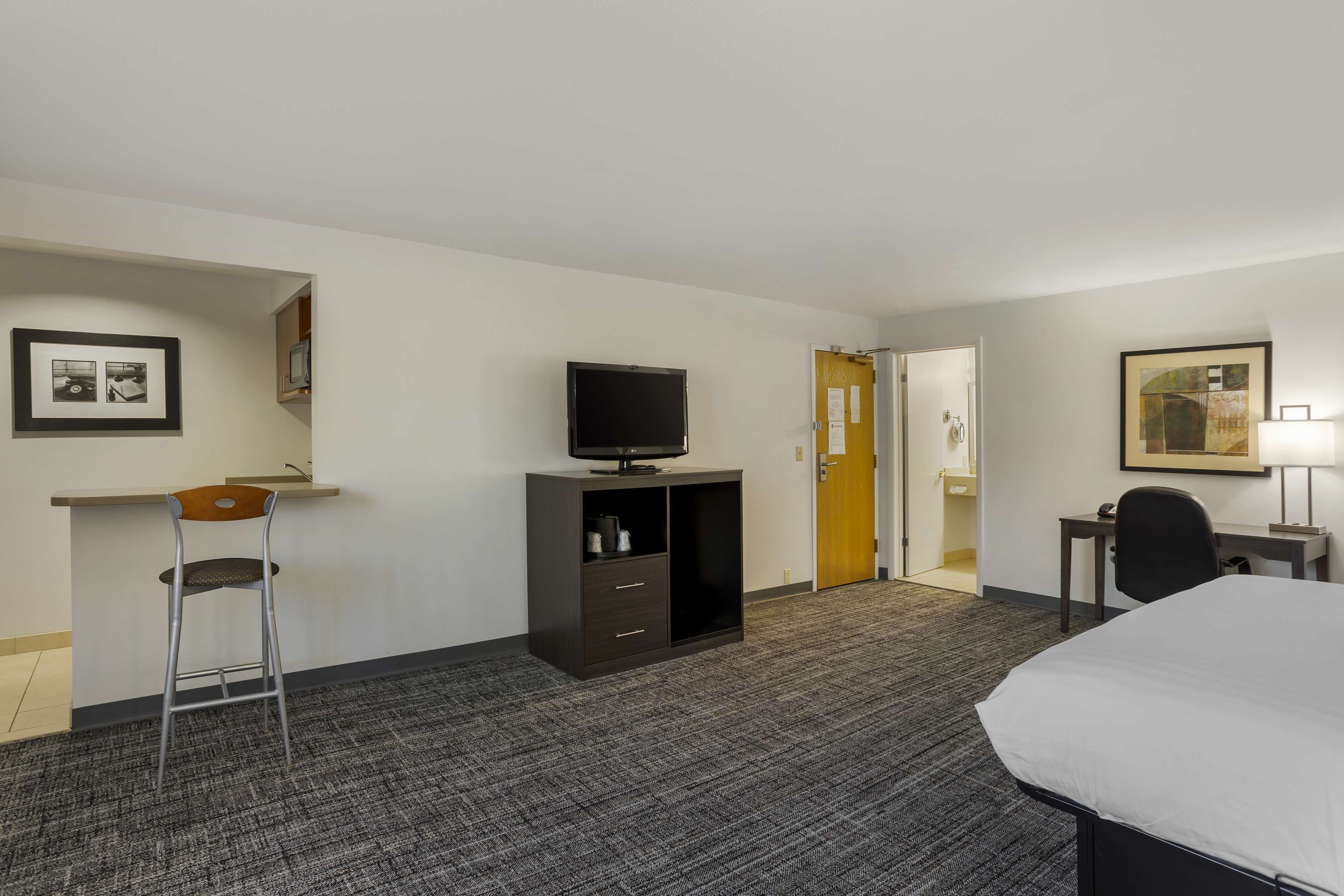 Une chambre d’hôtel avec un lit, un bureau et une chaise, un téléviseur posé sur un meuble, et une porte de salle de bain.