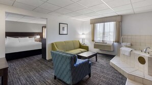 A hotel room with a bed, a sofa, a small table, a chair, a bathroom with a sink and bathtub, and a window with curtains. - Best Western DuBois Hotel (DuBois)