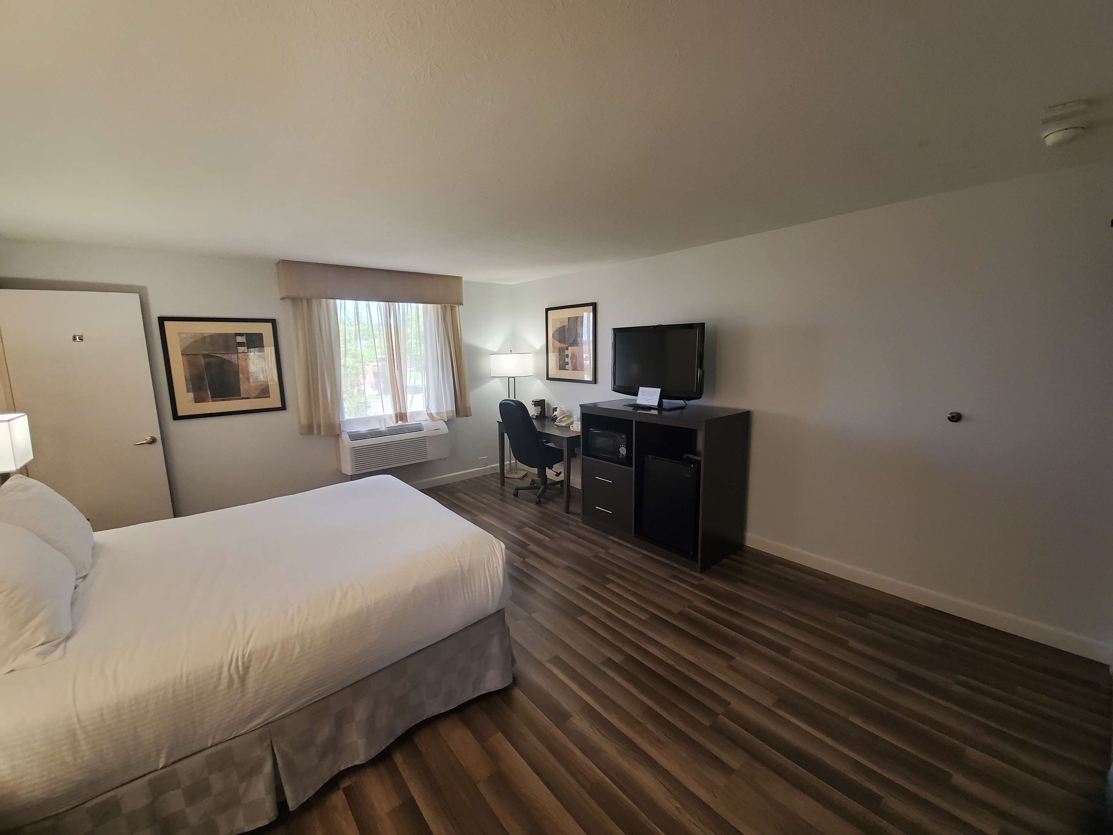 A hotel room with a bed, a desk, a television, and a window with curtains.