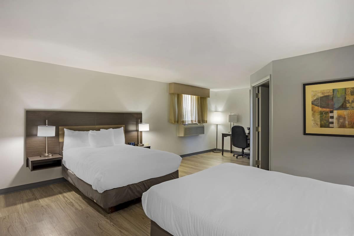 A hotel room with two beds, a desk, a chair, and a painting on the wall.