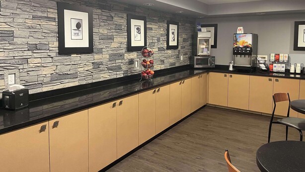 A modern kitchen with stone wall backsplash, framed artwork, a microwave, and a juice dispenser. - Best Western DuBois Hotel (DuBois)