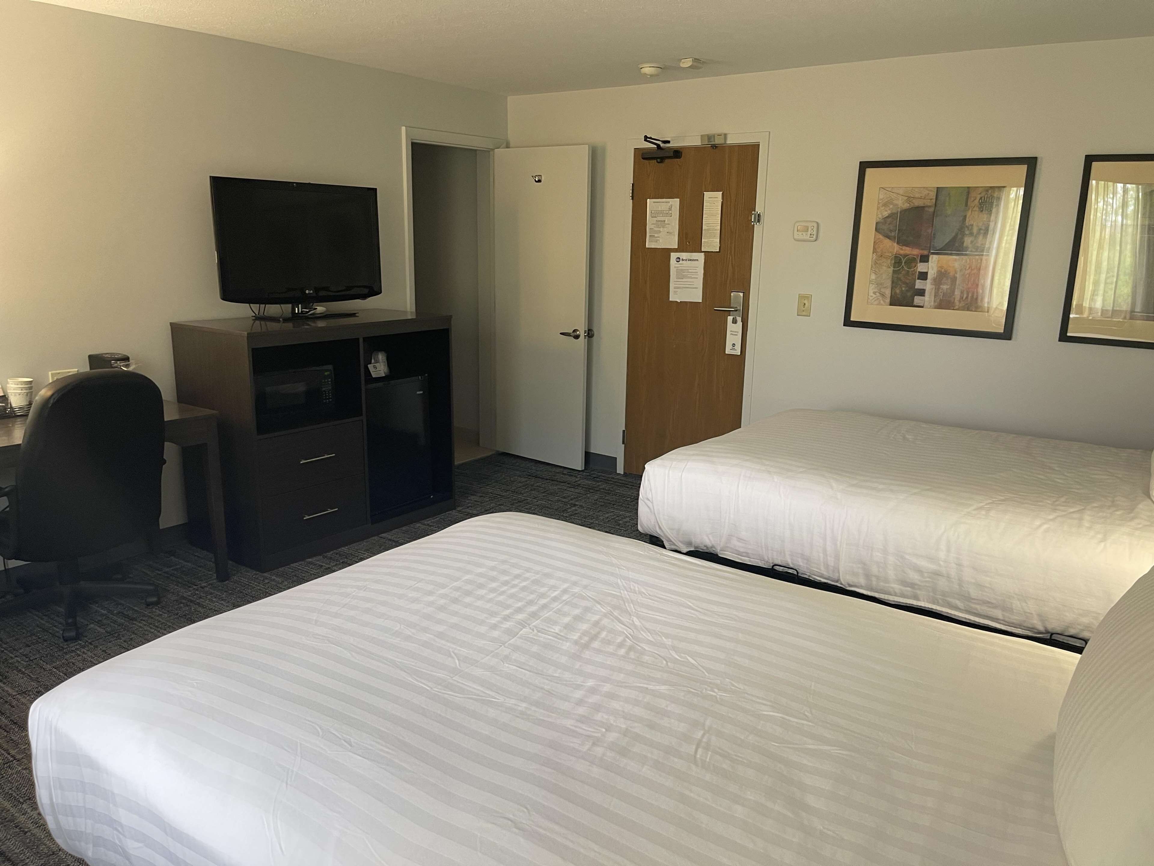 A hotel room with two beds, a desk with a television, a minibar, and a door with a lock.