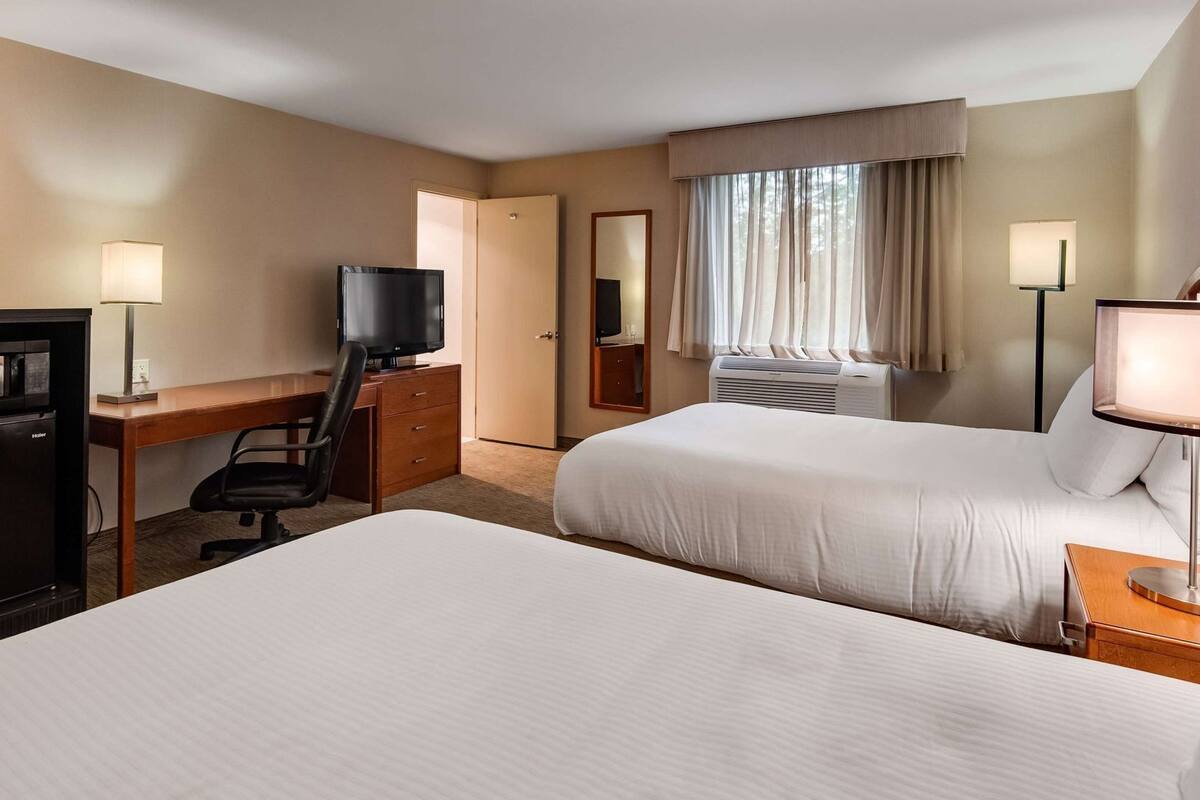 A hotel room with two beds, a desk, a television, a minibar, and a window with curtains.