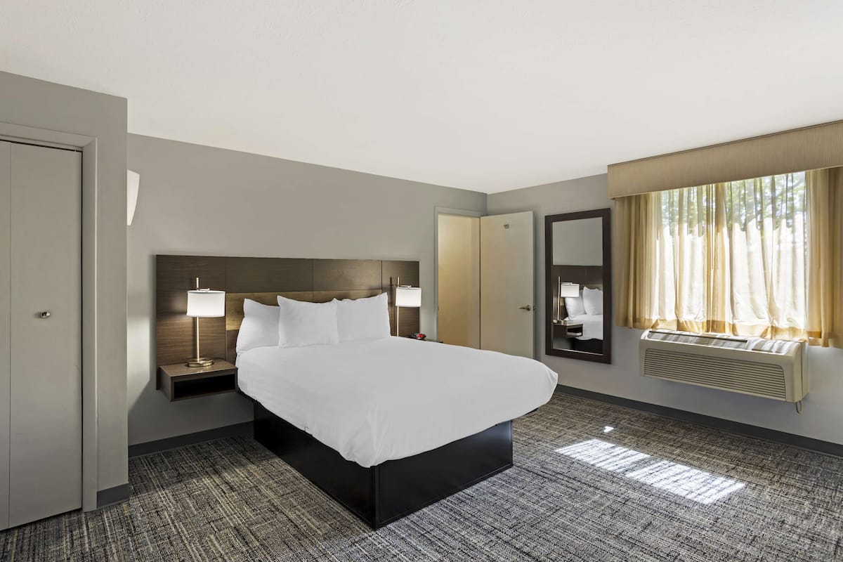 A hotel room with a large bed, bedside tables with lamps, a wardrobe, a mirror, and a window with curtains.