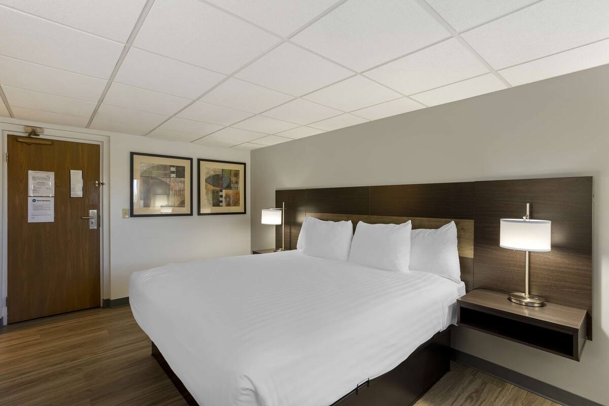 A hotel room with a large bed, two bedside tables with lamps, wooden headboard, and two framed pictures on the wall.