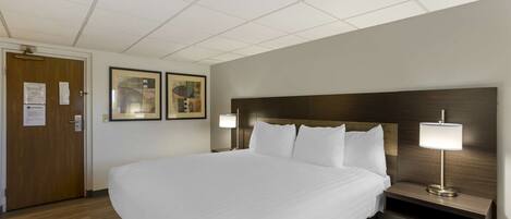 A hotel room with a large bed, two bedside tables with lamps, wooden headboard, and two framed pictures on the wall.