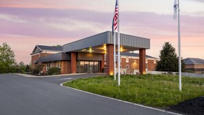A modern building with a covered entrance, two flagpoles, and a landscaped area with grass and trees. - Best Western DuBois Hotel (DuBois)